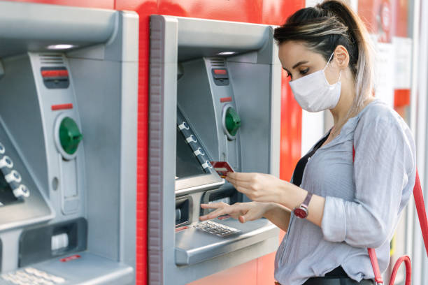 Young woman wearing protective face mask while withdrawing money at ATM Young woman wearing protective face mask while withdrawing money at ATM